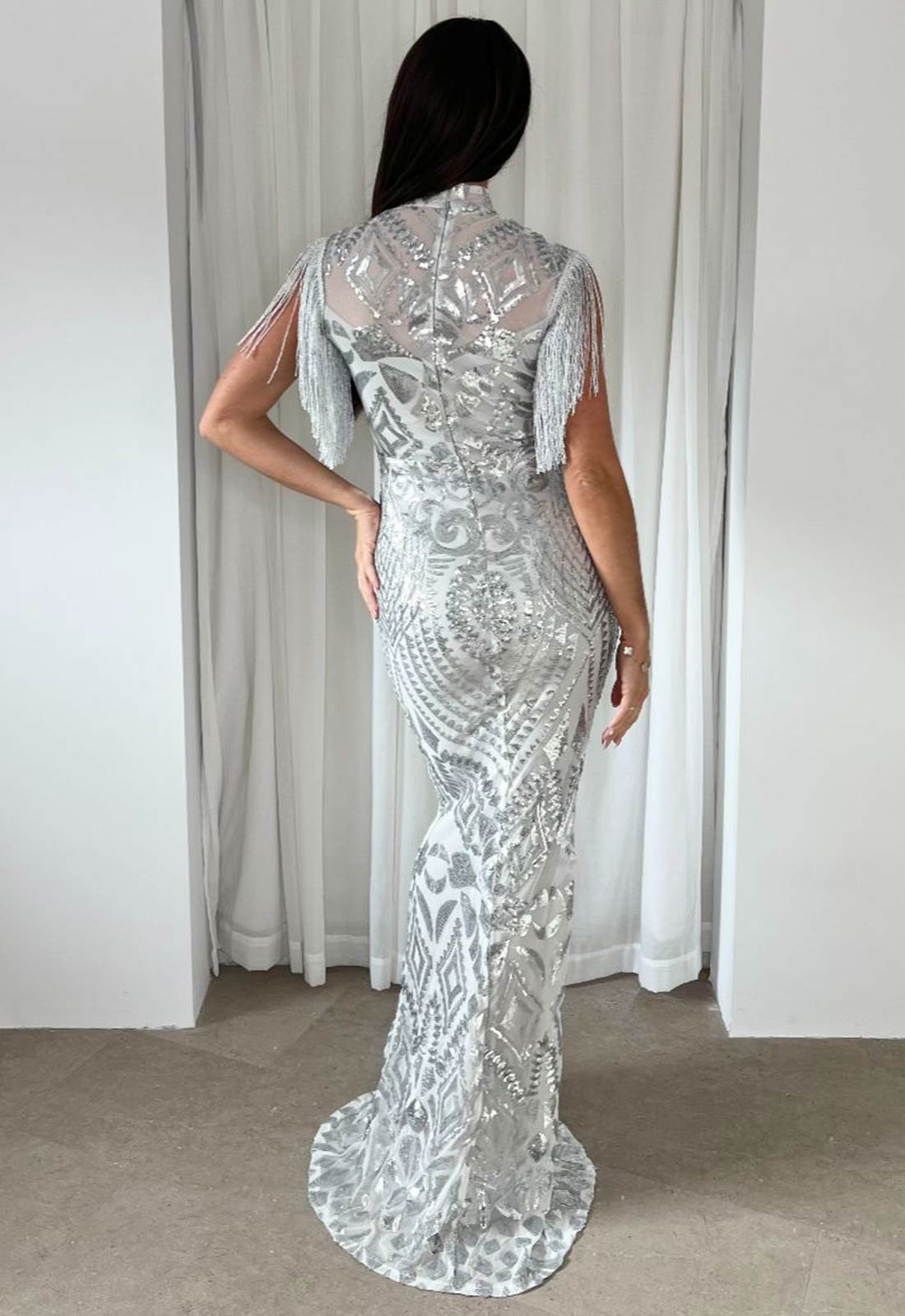 Woman wearing a silver sequin evening gown against a white curtain background