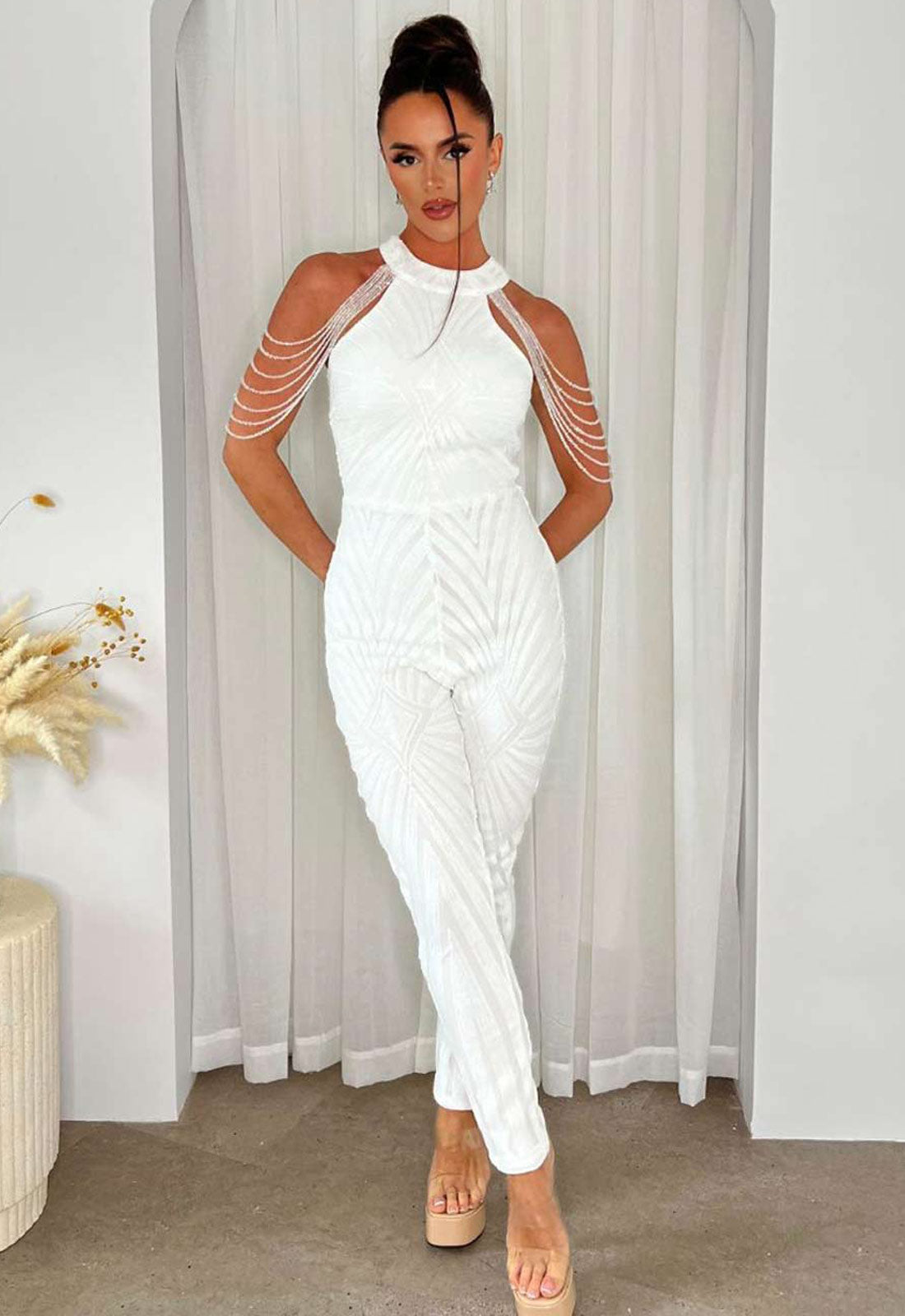 Woman wearing a white jumpsuit with sheer sleeves against a neutral background