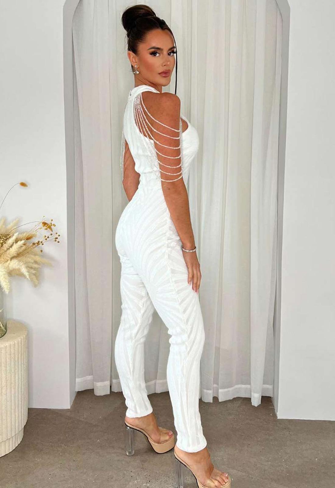 Woman wearing a white outfit with embellishments in a neutral setting