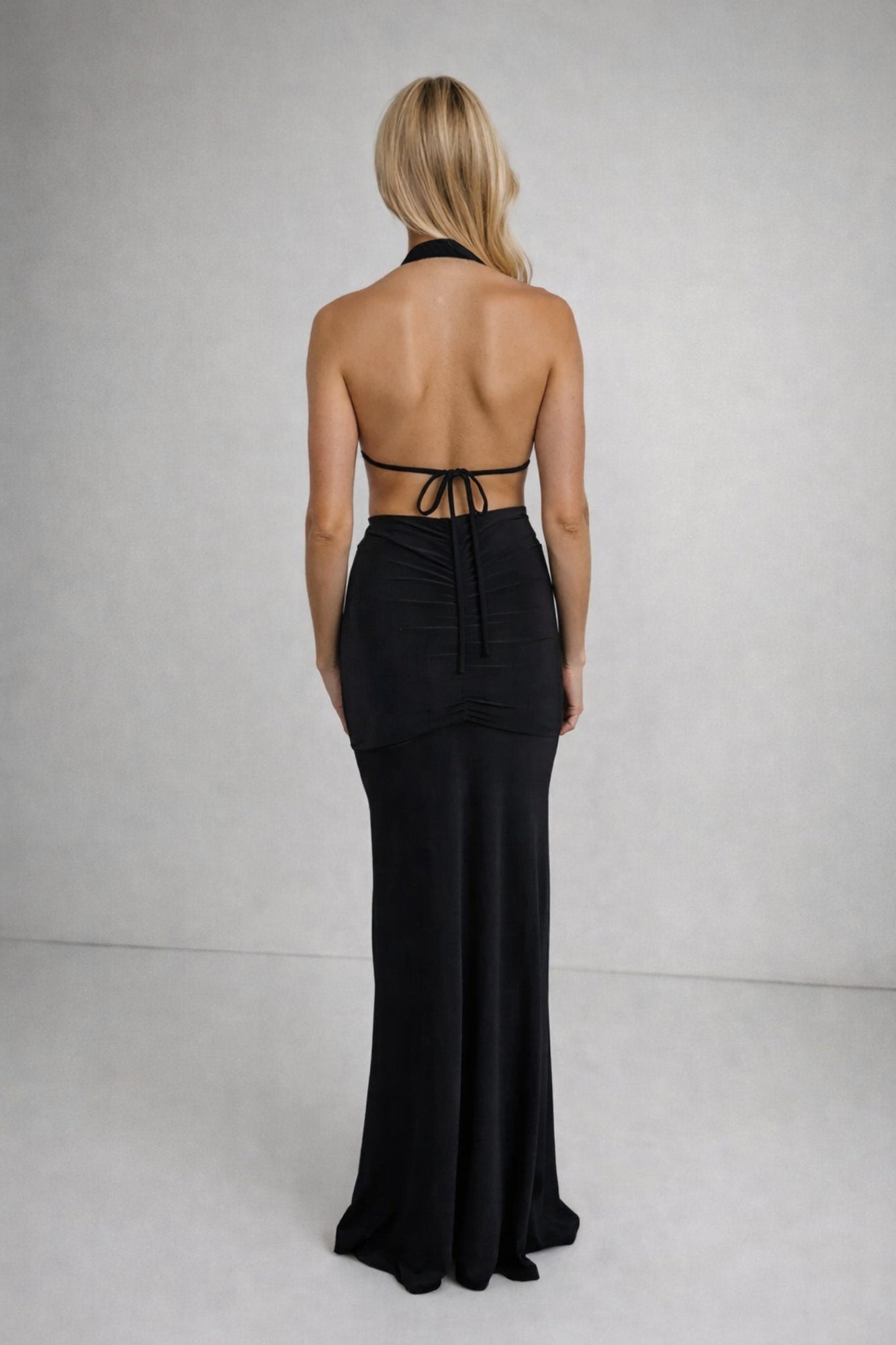 Black halter neck dress with open back on a plain background