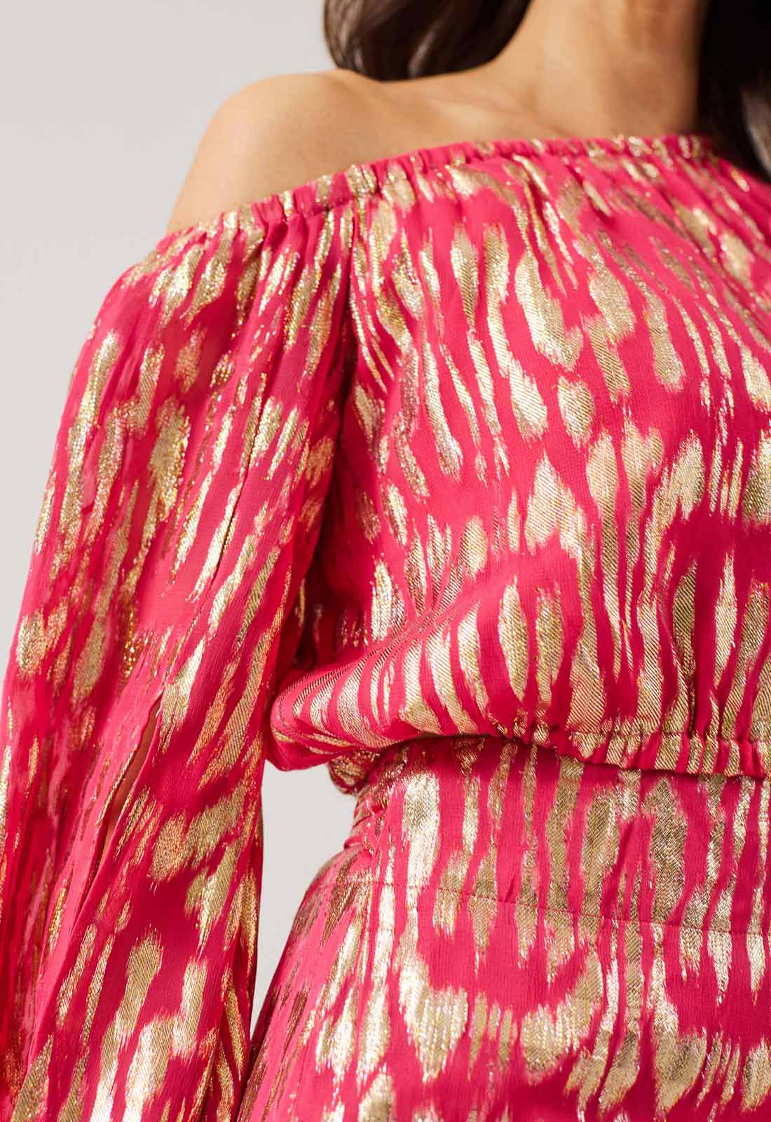 Close-up of a pink and gold patterned dress with off-shoulder design.