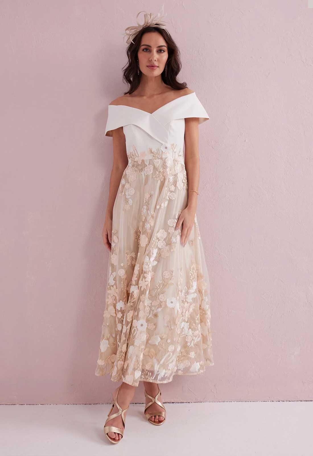 Woman wearing a white off-shoulder top and floral skirt against a pink background