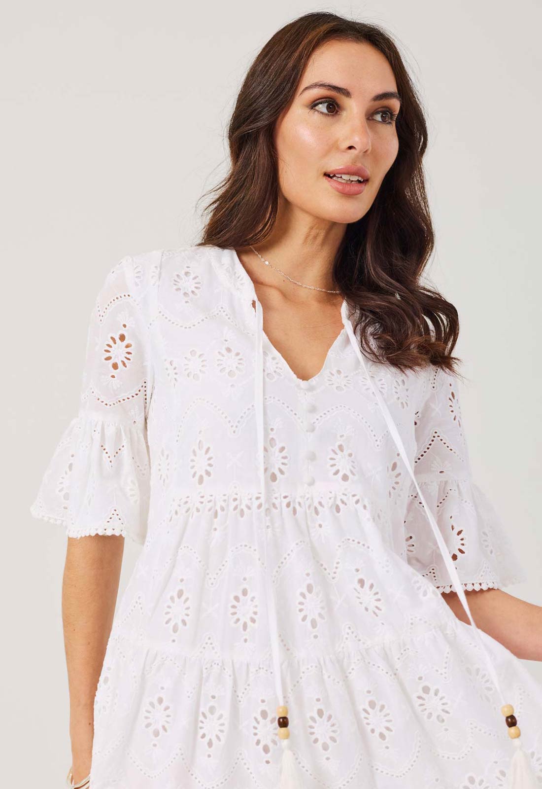 Woman wearing a white dress with lace details against a plain background