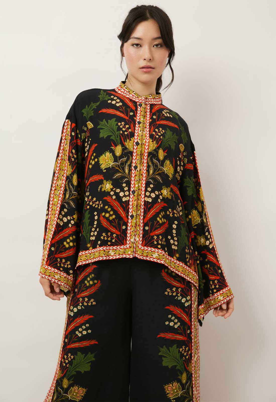 Woman wearing a black embroidered top with colorful patterns on a white background