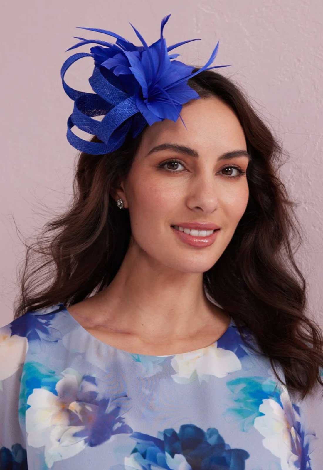 Woman wearing a blue feathered headpiece against a pink background