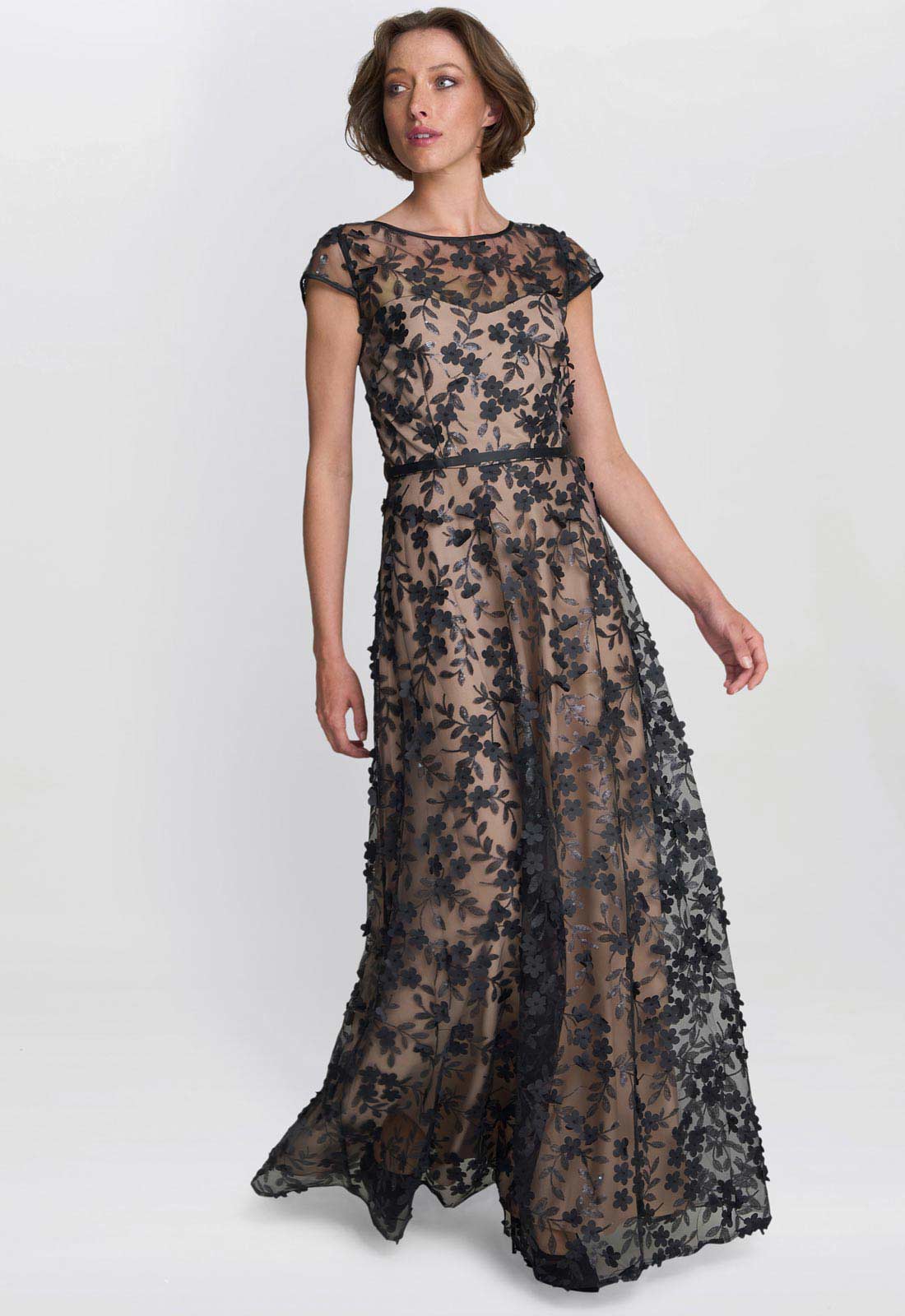Woman wearing a long, dark floral lace dress on a white background