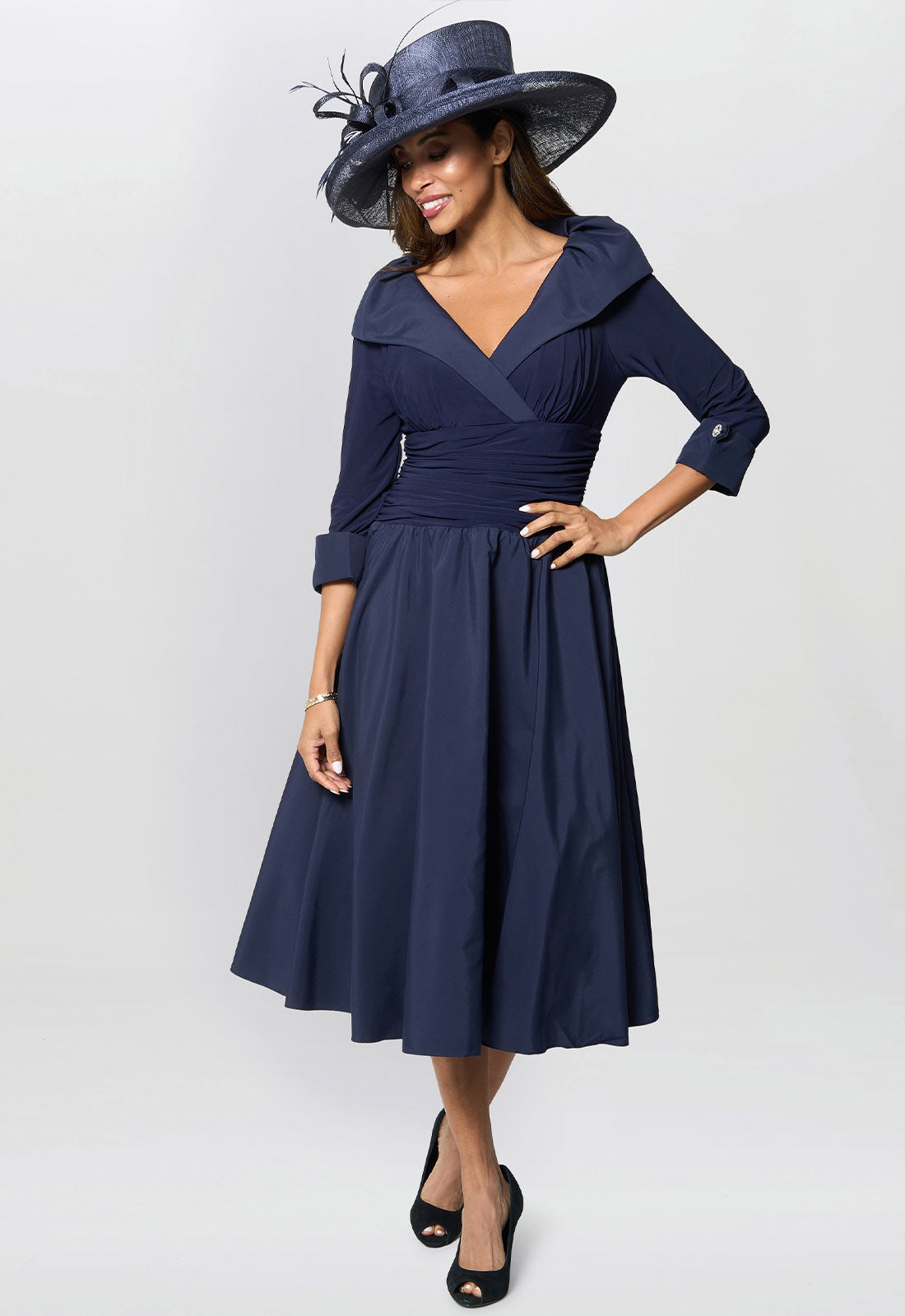 Woman wearing a navy blue dress with a matching hat on a white background