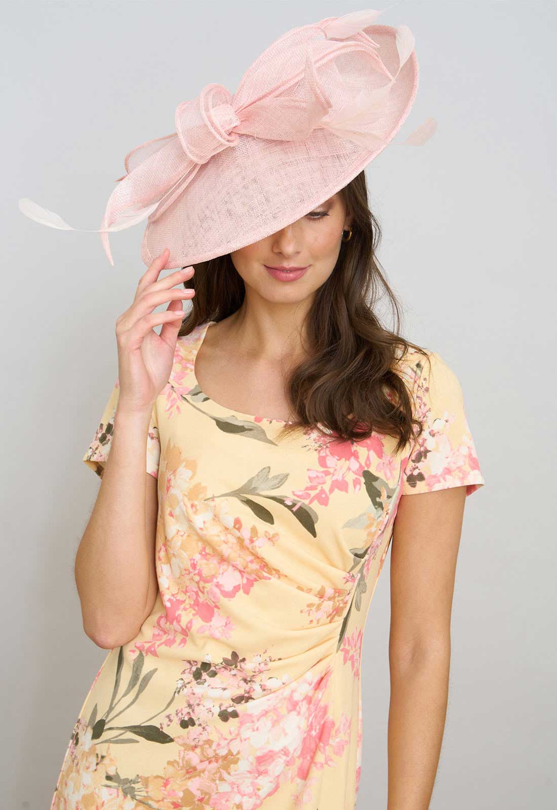 Woman wearing a pink floral dress and matching hat against a gray background
