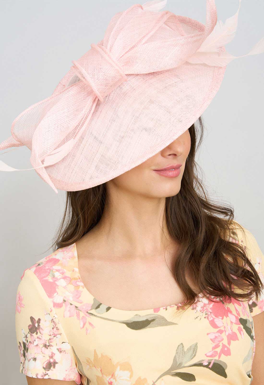 Woman wearing a large pink hat with a bow, against a plain background