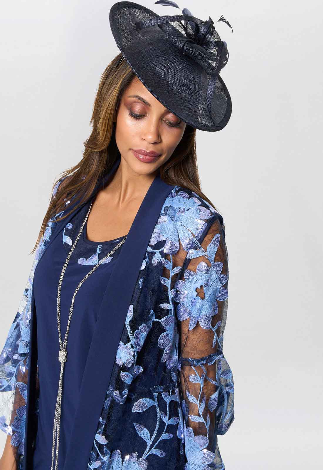 Woman wearing a navy dress with floral pattern and matching hat against a white background
