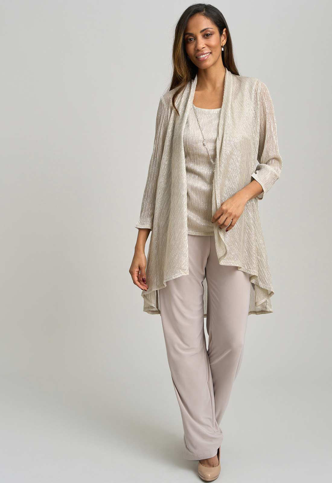 Woman wearing a beige outfit with a matching cardigan on a plain background