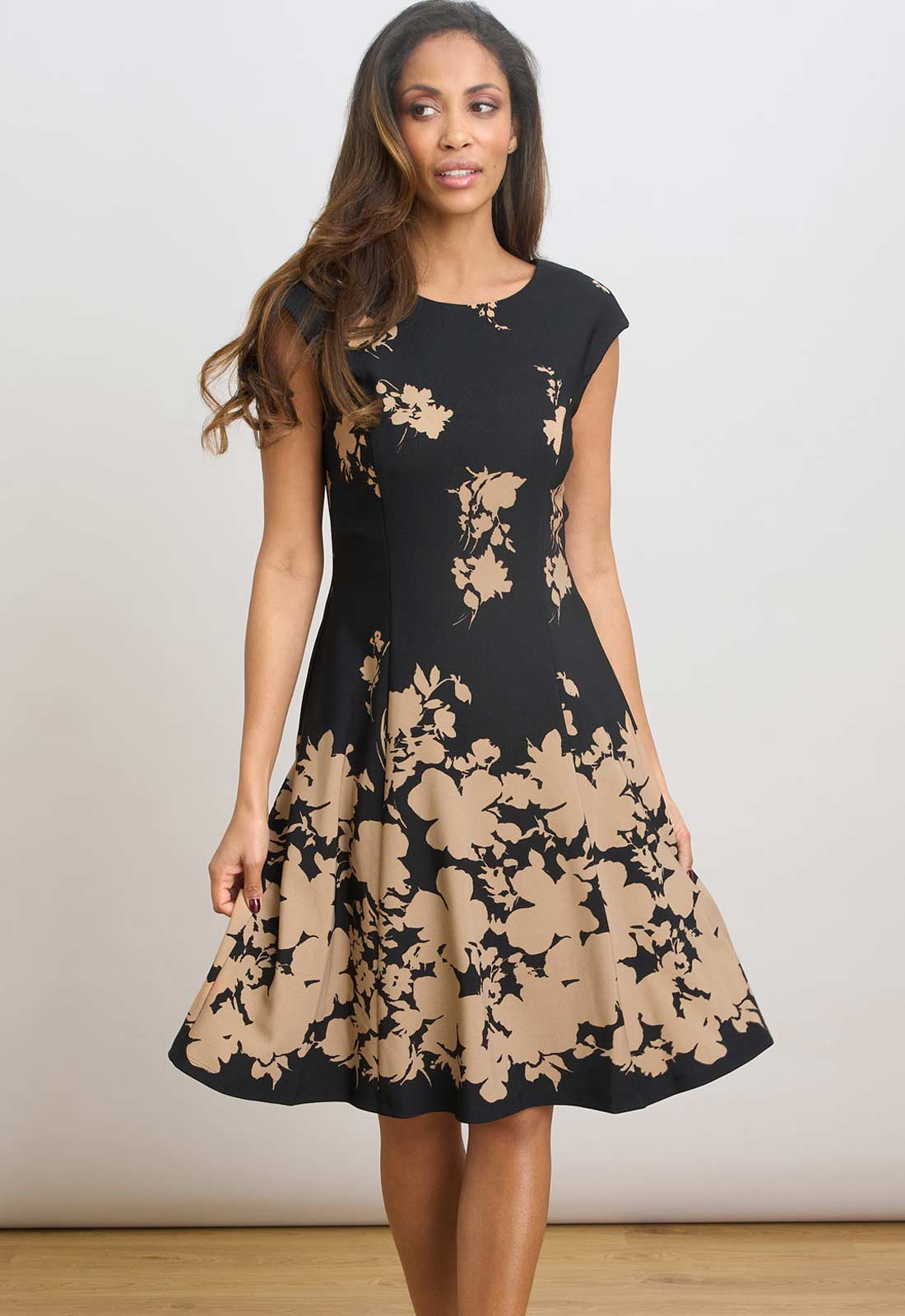 Woman wearing a black and beige floral dress against a plain background