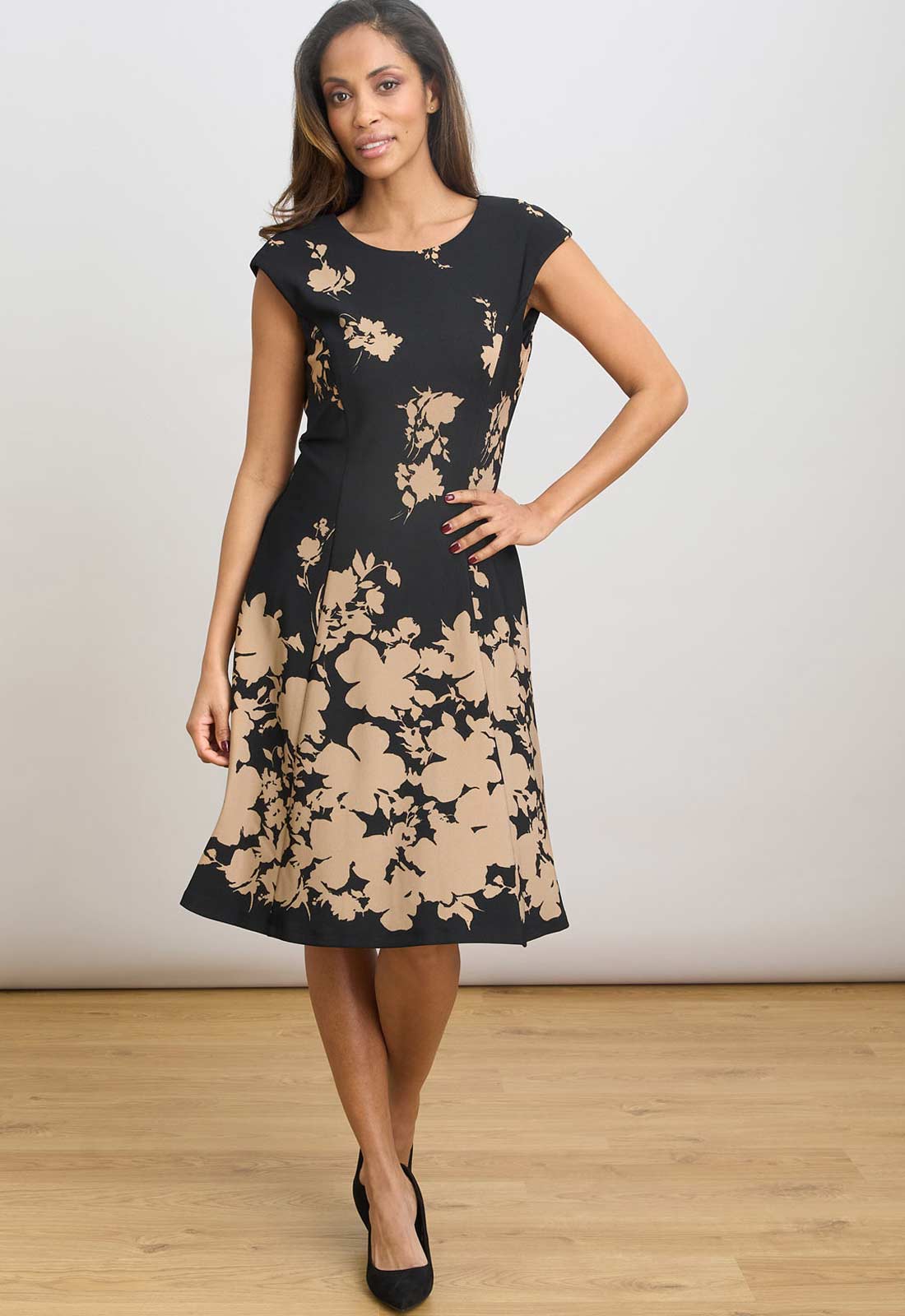 Woman wearing a black dress with beige floral patterns on a plain background