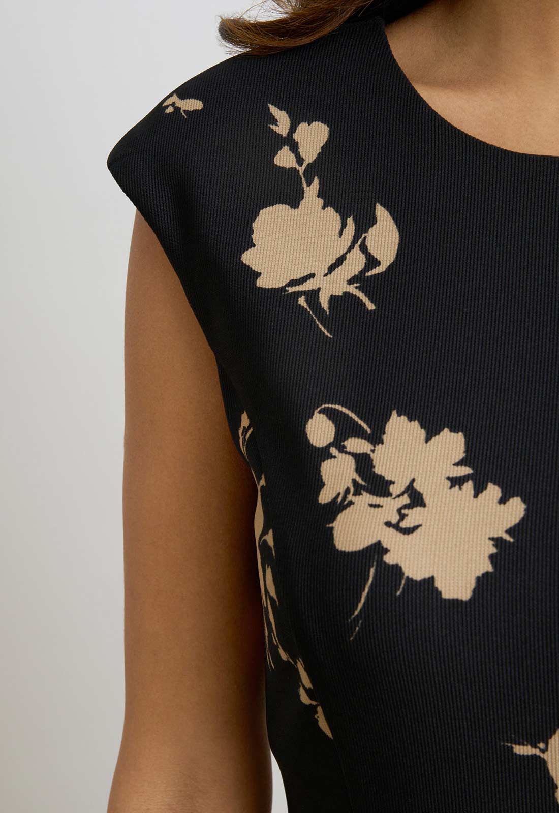 Black sleeveless top with beige floral patterns on a plain background