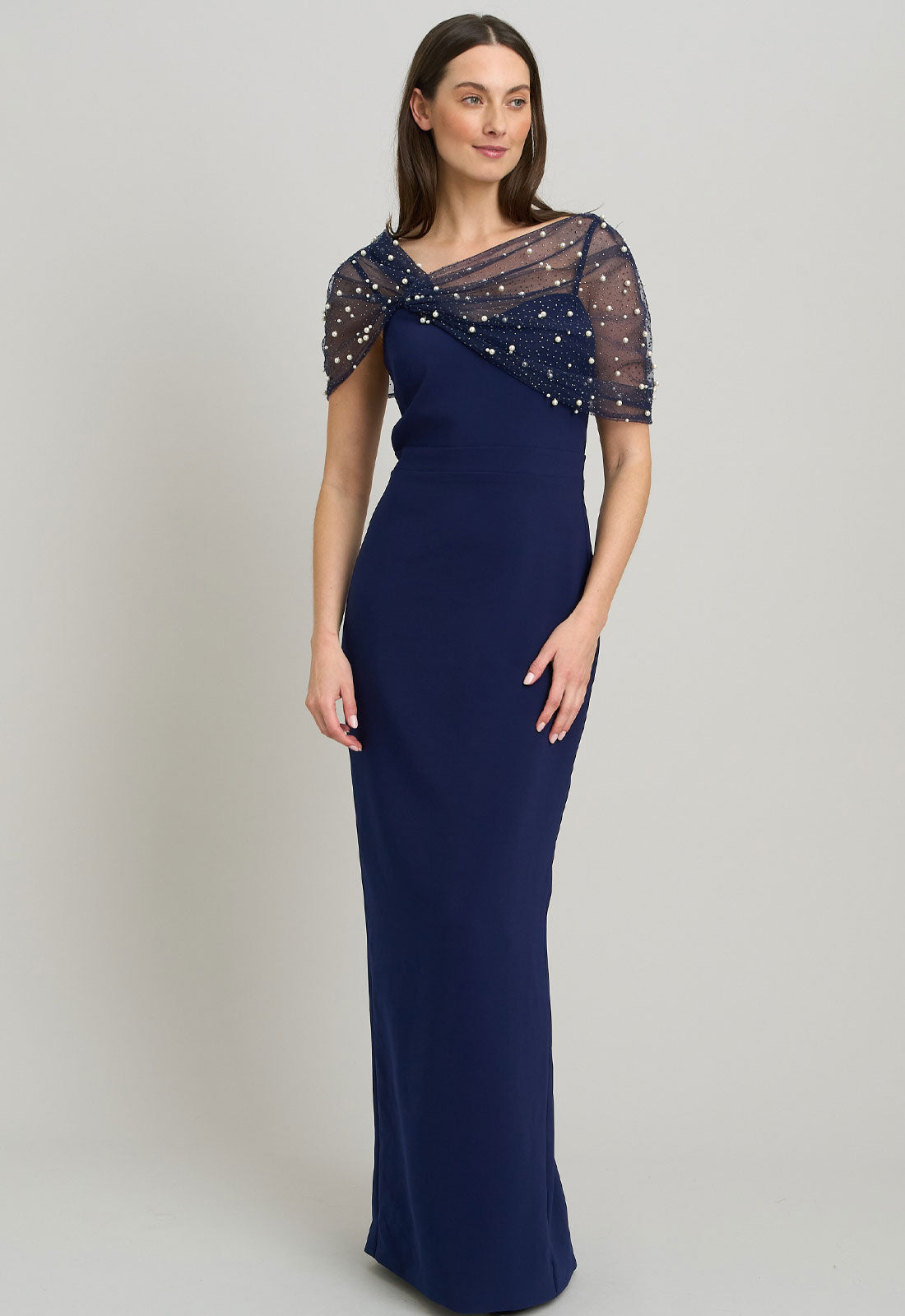 Navy evening gown with sheer sleeves and beading on a plain background