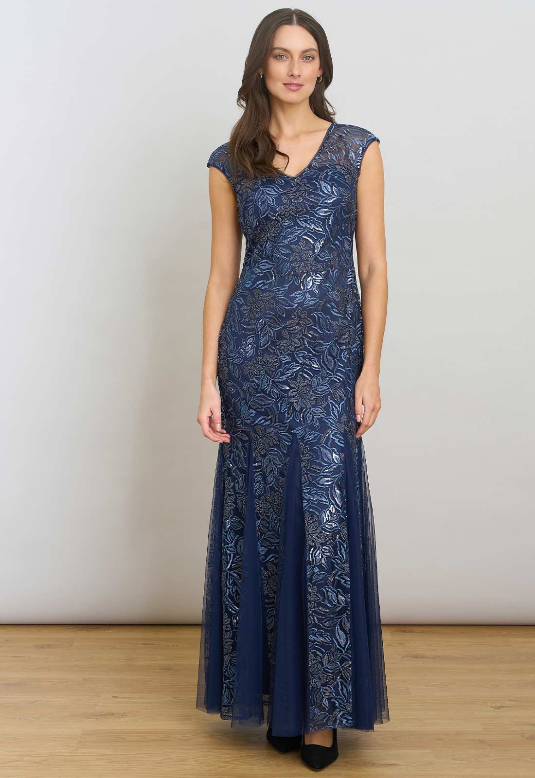 Woman wearing a long blue lace dress against a plain background