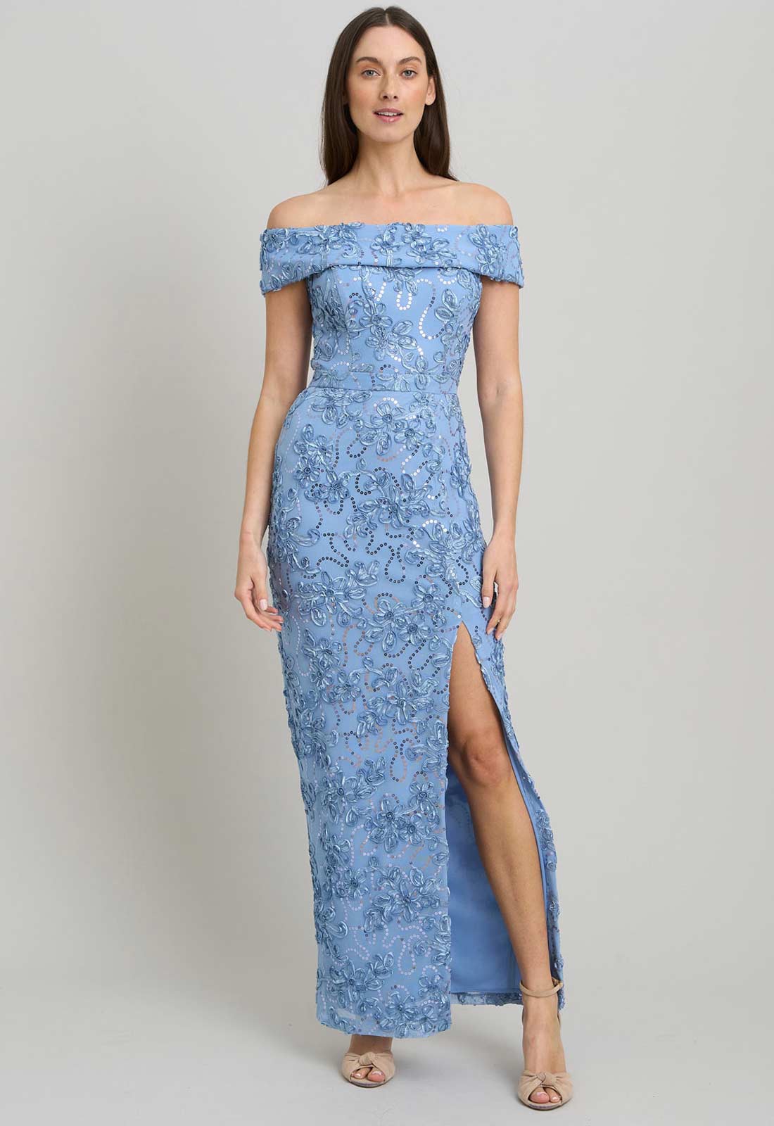 Woman wearing a blue off-shoulder lace dress with a slit on a gray background