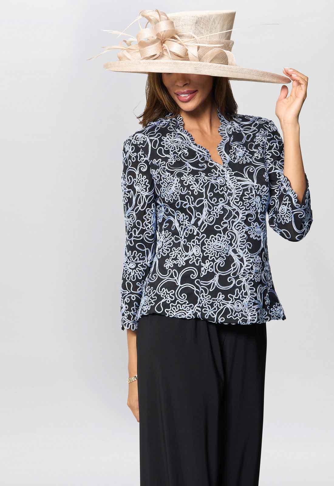 Woman wearing a black and white patterned blouse with a wide-brimmed beige hat on a white background