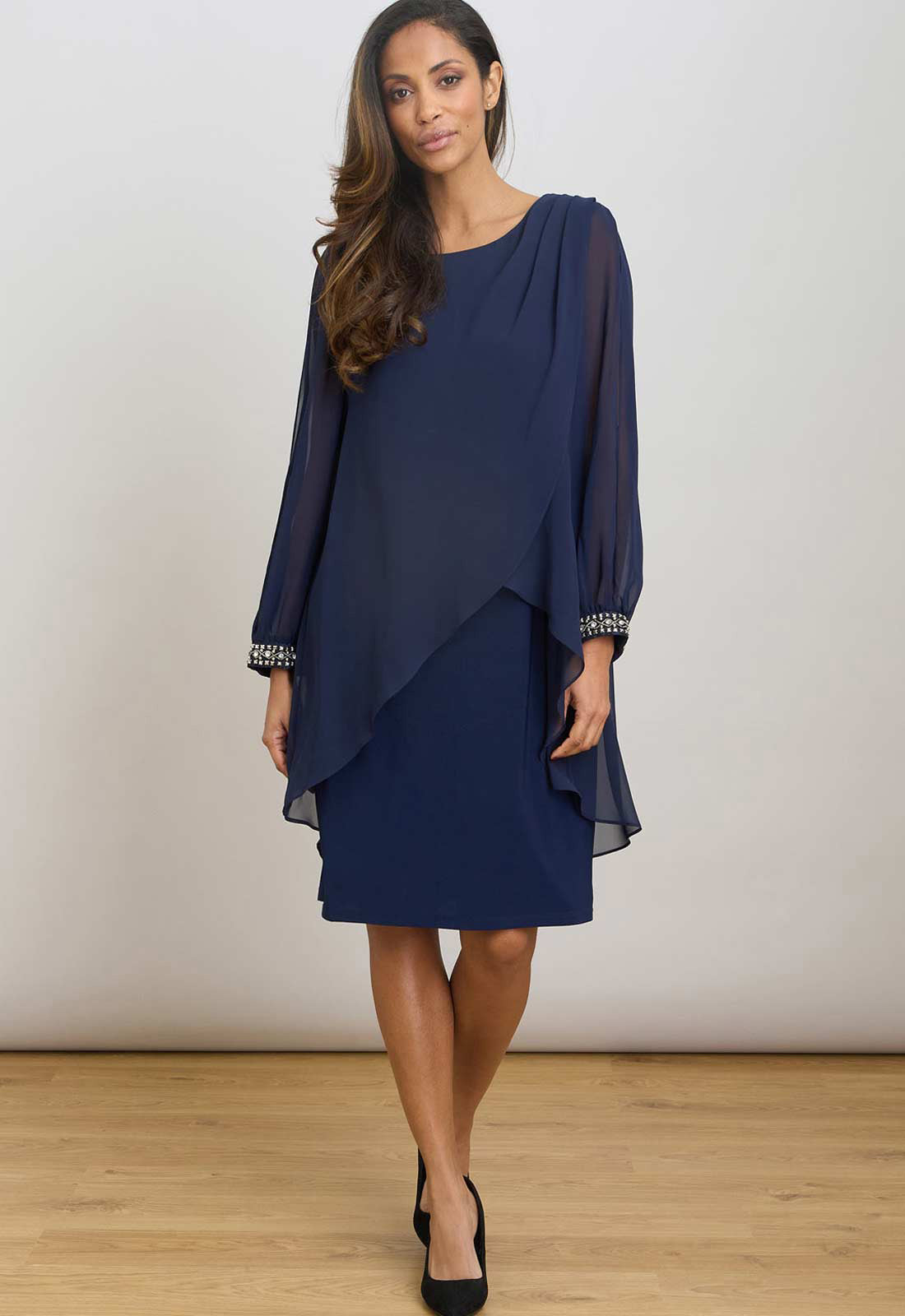 Woman wearing a navy blue dress with sheer sleeves against a white background