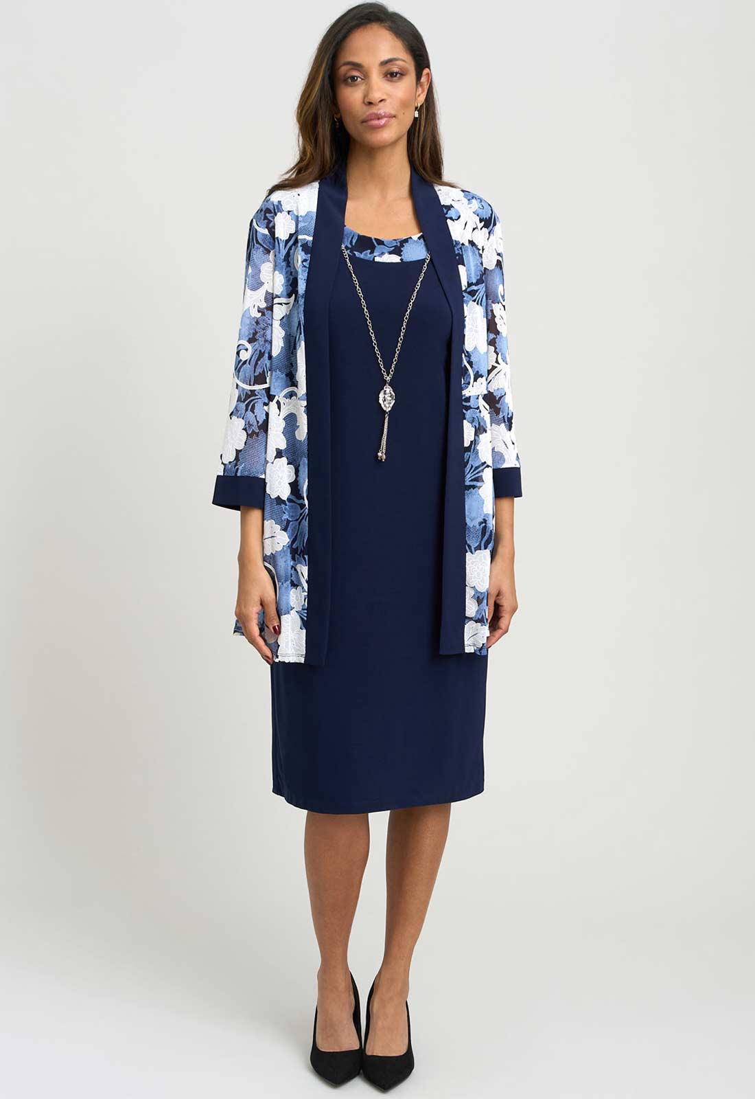 Woman wearing a navy dress with a floral cardigan on a white background