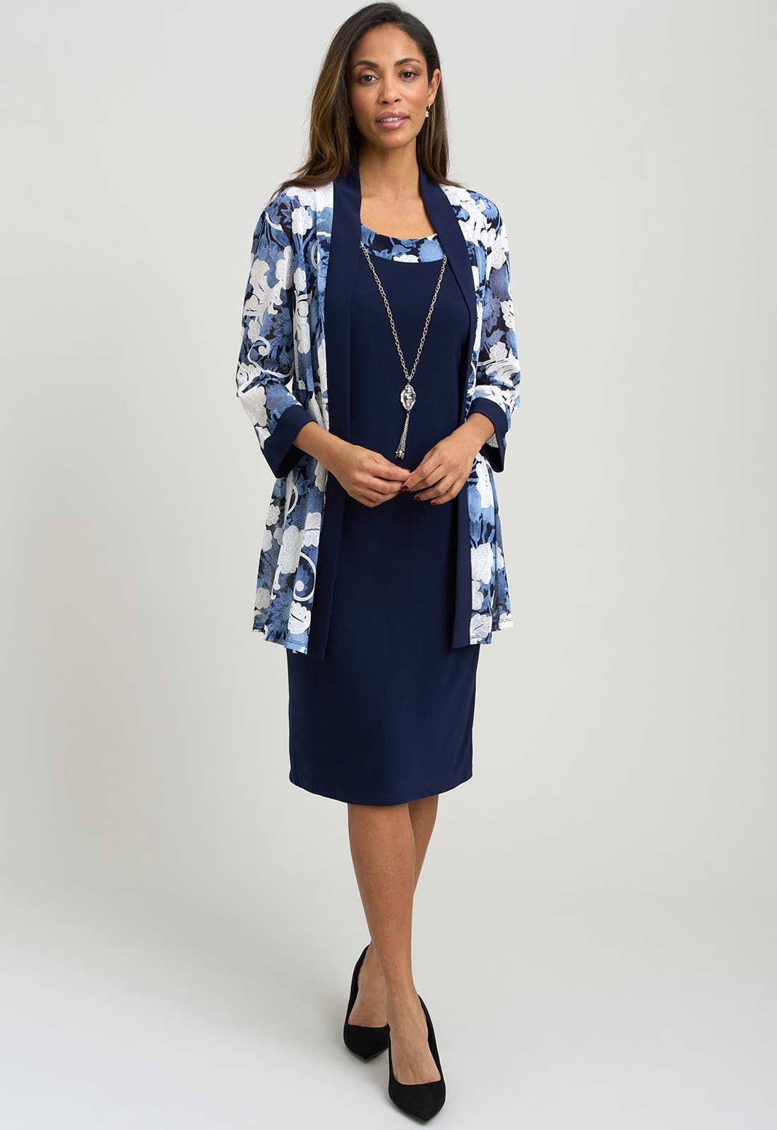 Woman wearing a navy dress with a floral jacket on a white background