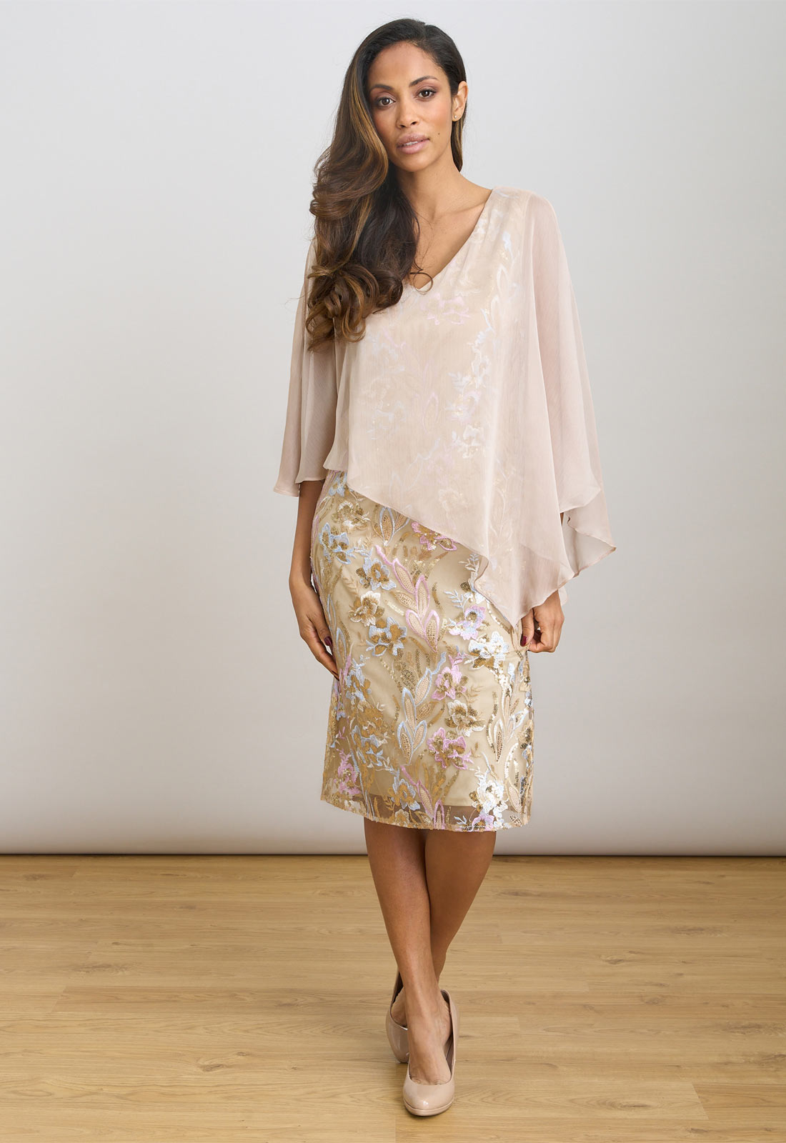 Woman wearing a beige top and floral skirt against a white background