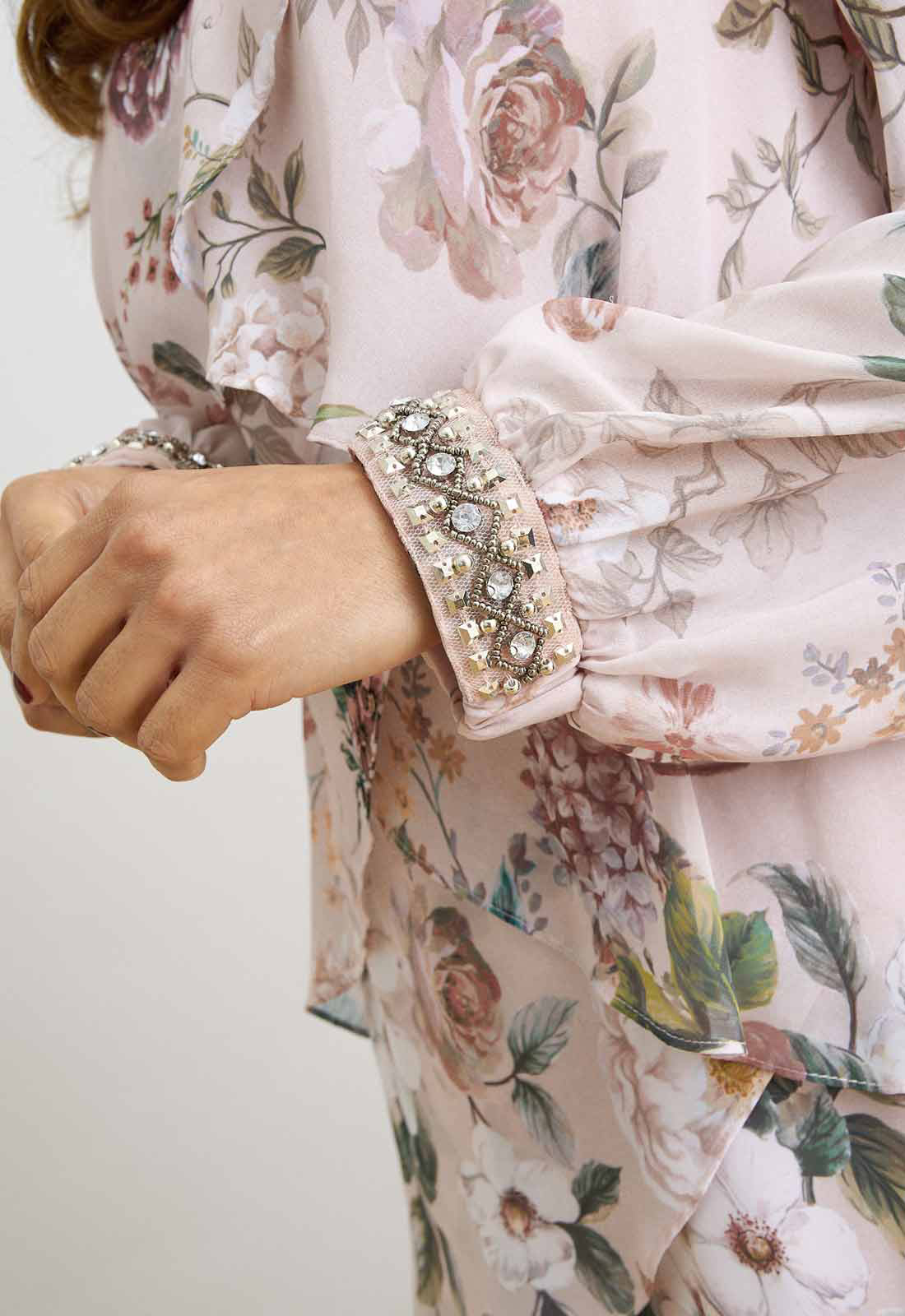 Close-up of a floral dress with embellished cuffs on a plain background