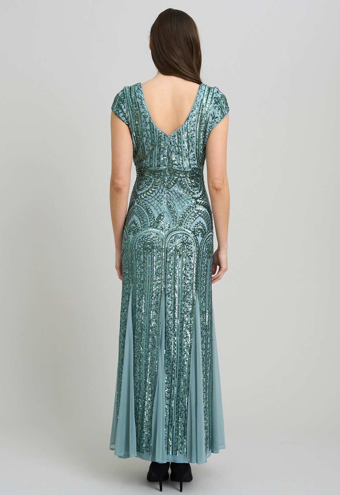 Woman wearing a long, patterned teal dress on a plain background
