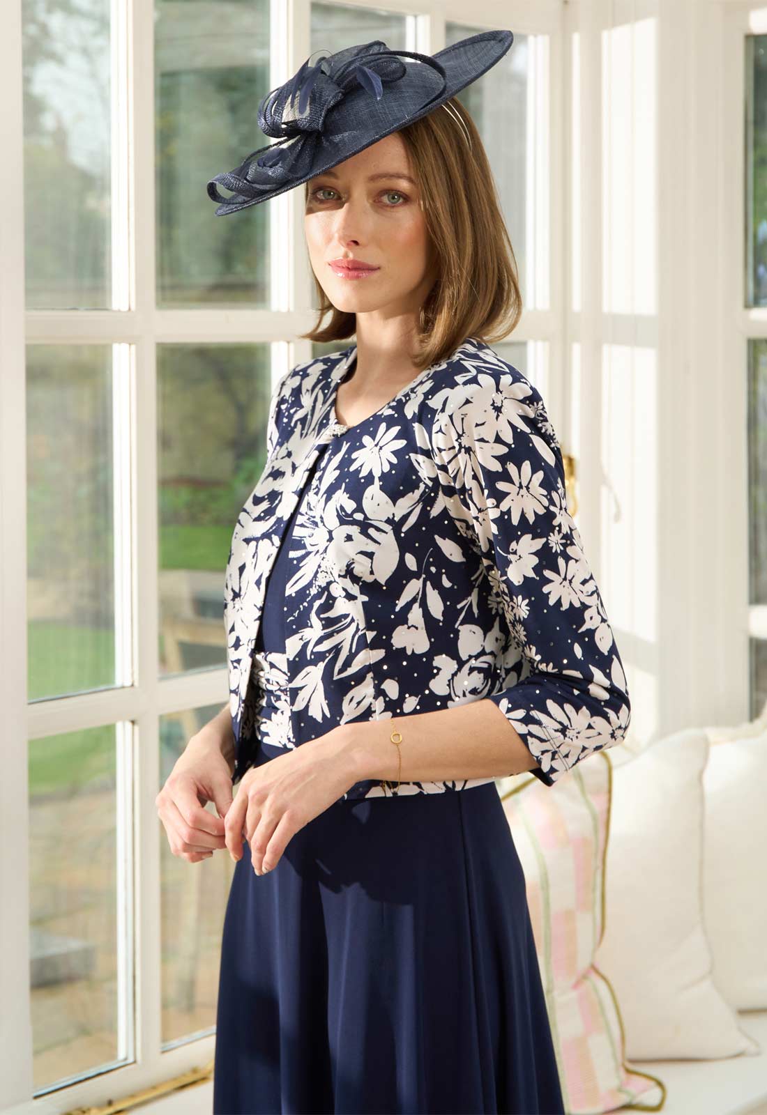 Woman wearing a navy and white floral outfit with a matching hat indoors.
