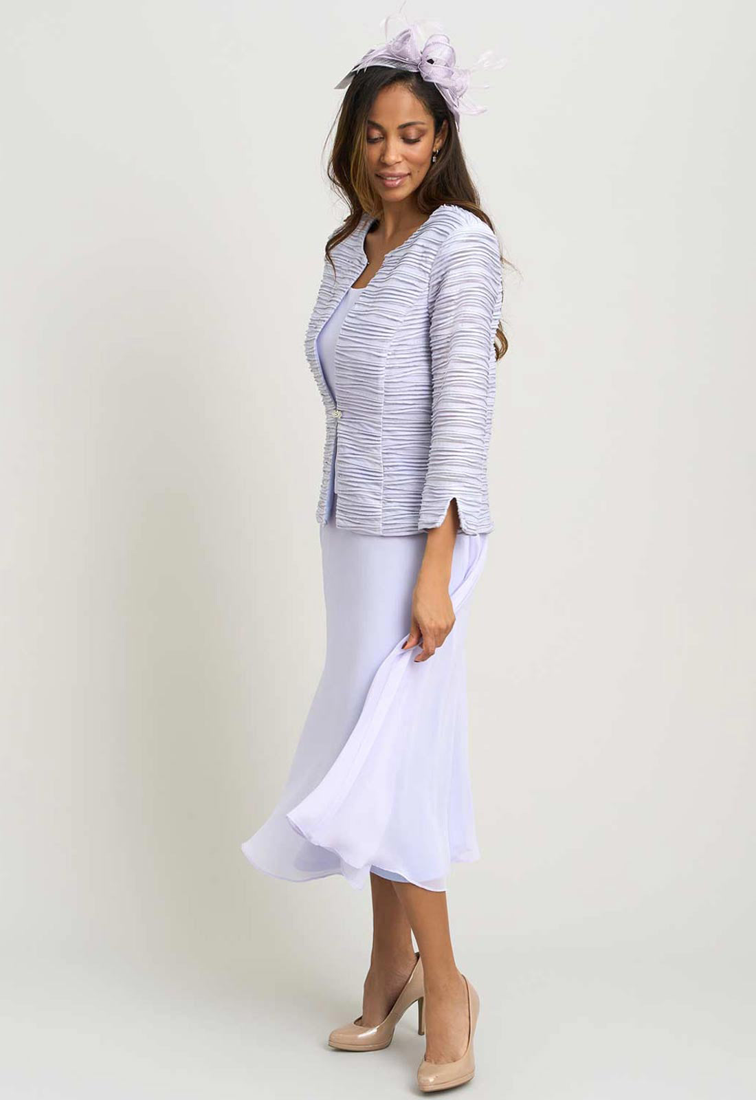 Woman wearing a white dress with a matching jacket on a plain background