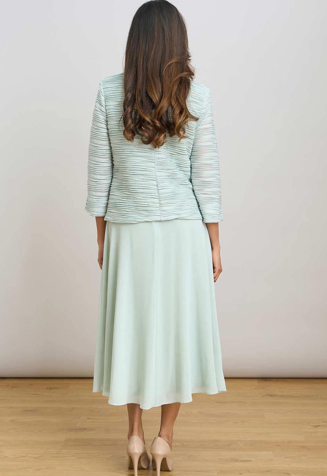Woman wearing a light green jacket and skirt set on a plain background