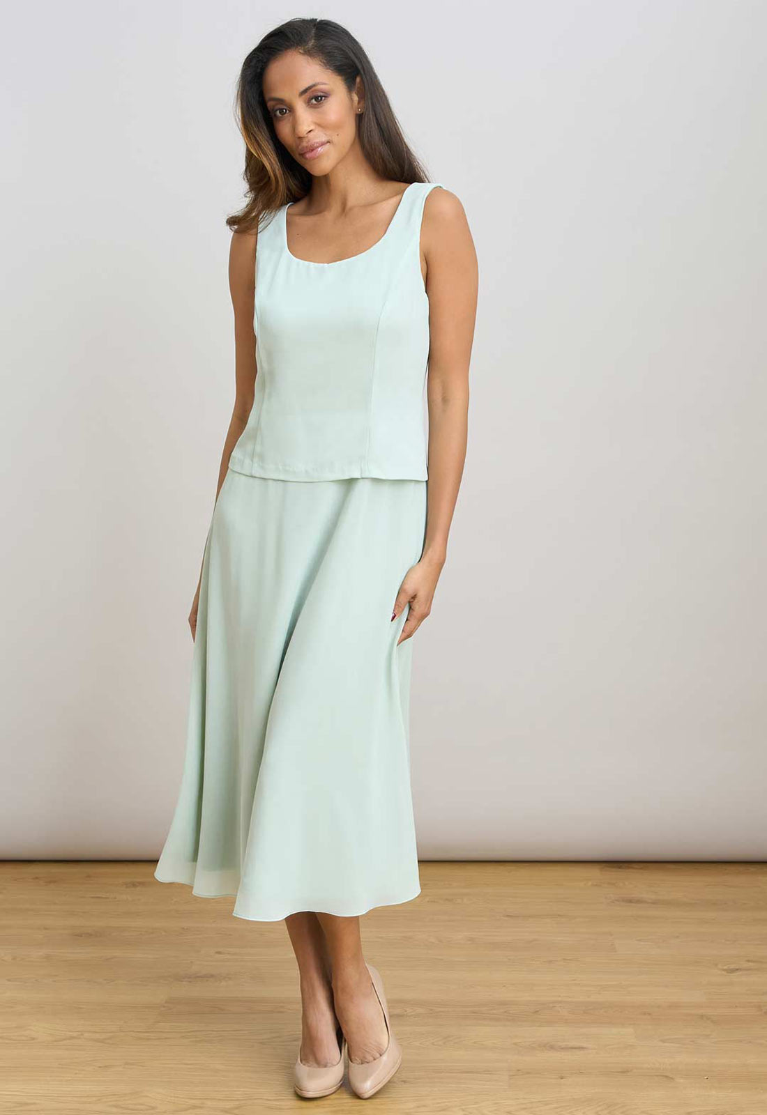 Woman wearing a light green sleeveless top and skirt set on a plain background