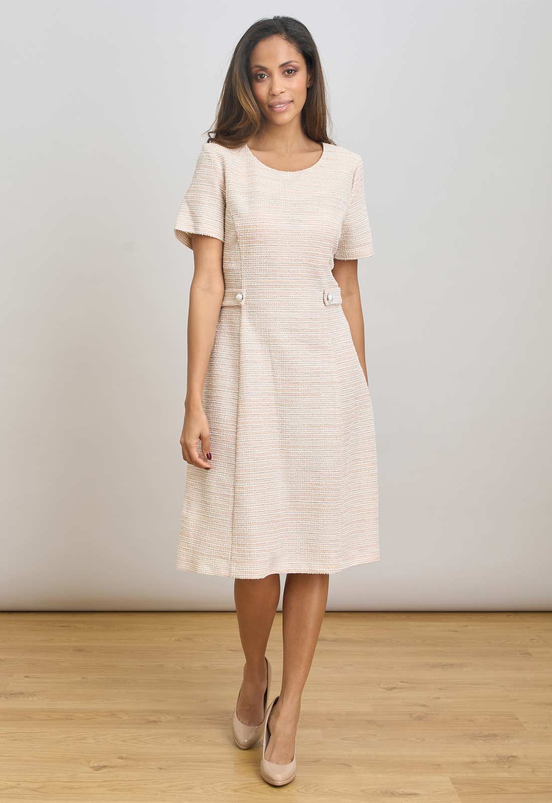 Woman wearing blush pink dress standing against a plain background