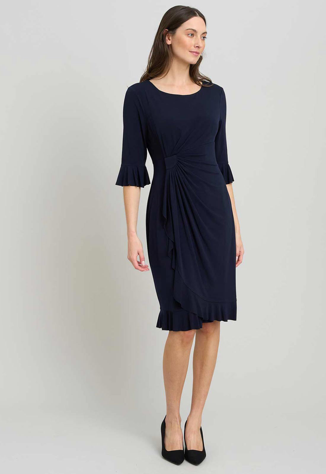 Woman wearing a navy blue dress with ruffled sleeves and hem on a light gray background