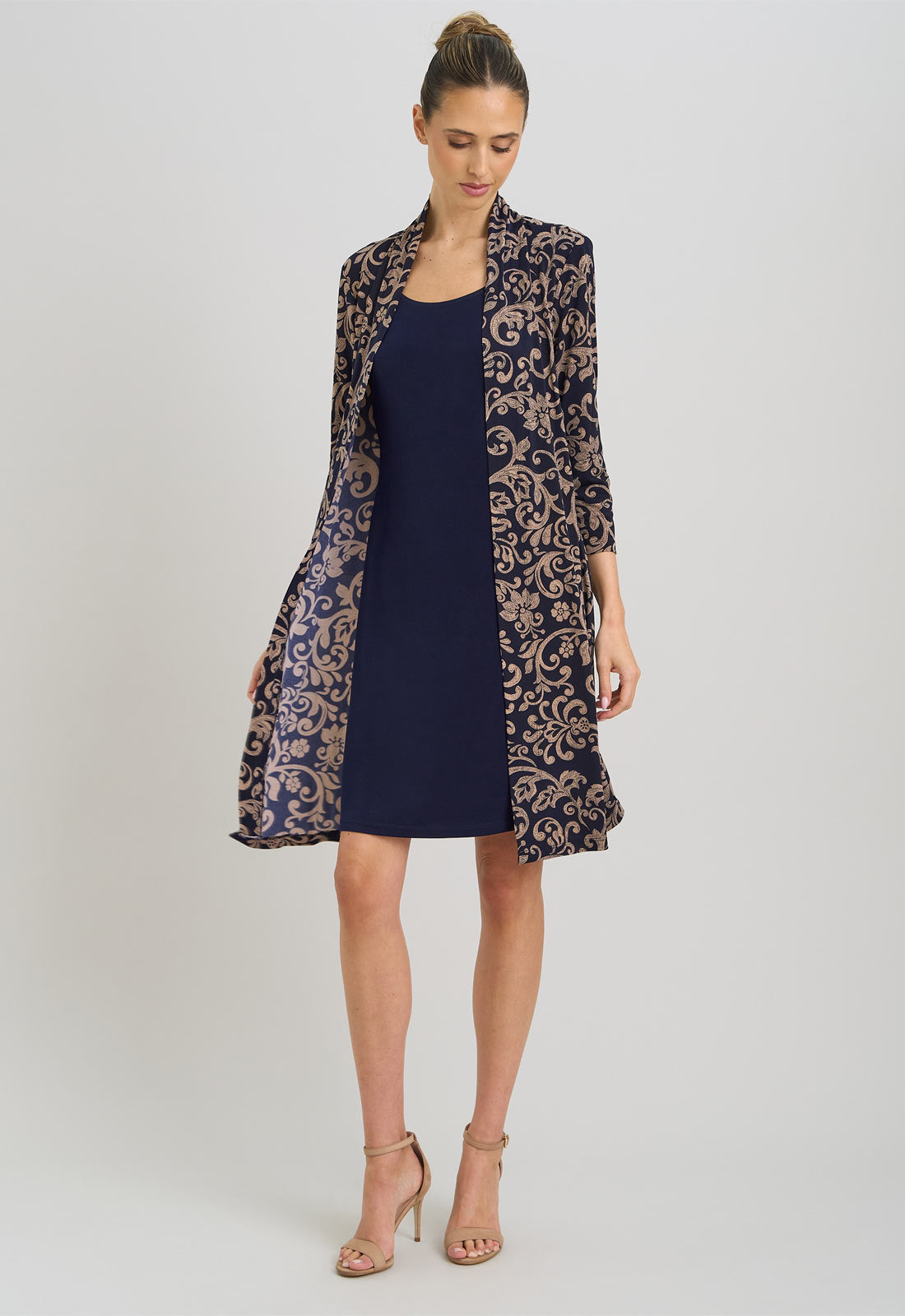 Woman wearing a navy dress with a patterned long coat on a light gray background