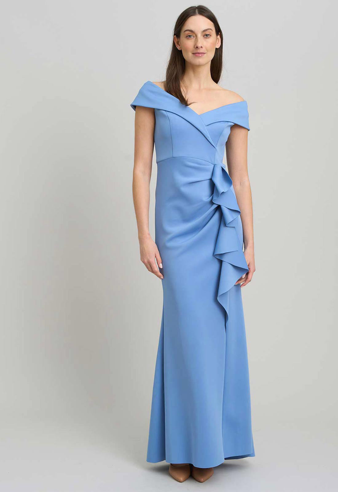 Woman wearing a blue off-shoulder gown with ruffle details on a gray background