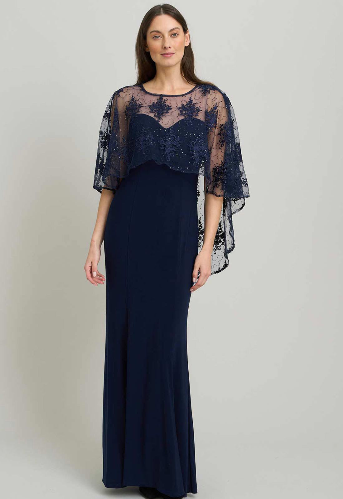 Woman wearing a navy evening gown with a lace overlay on a plain background
