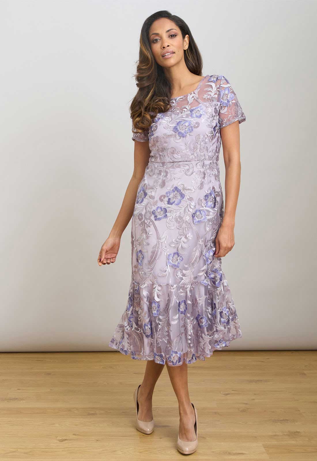 Woman wearing a floral dress standing on a wooden floor with a white background