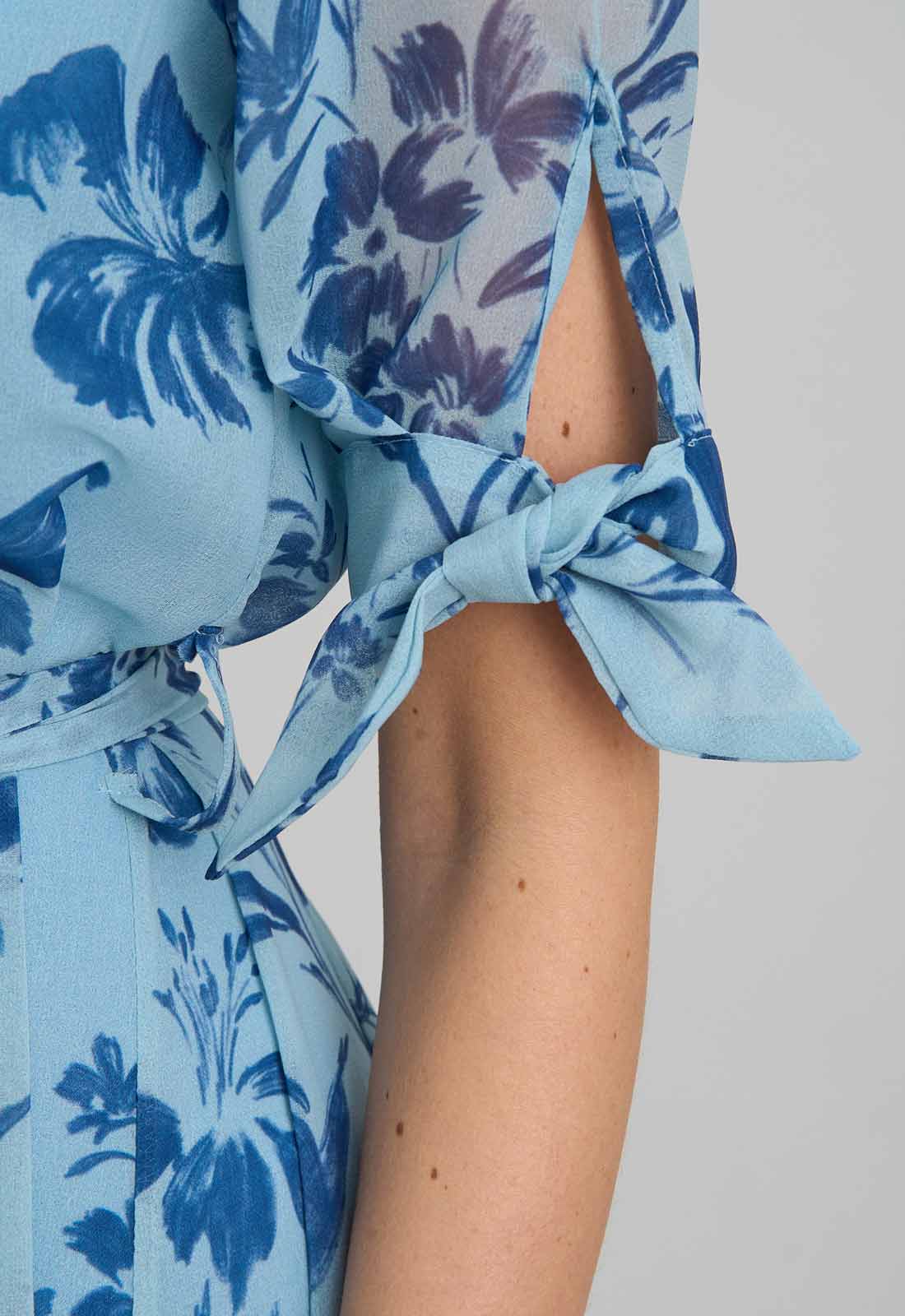 Close-up of a blue floral dress with a knot detail on a plain background