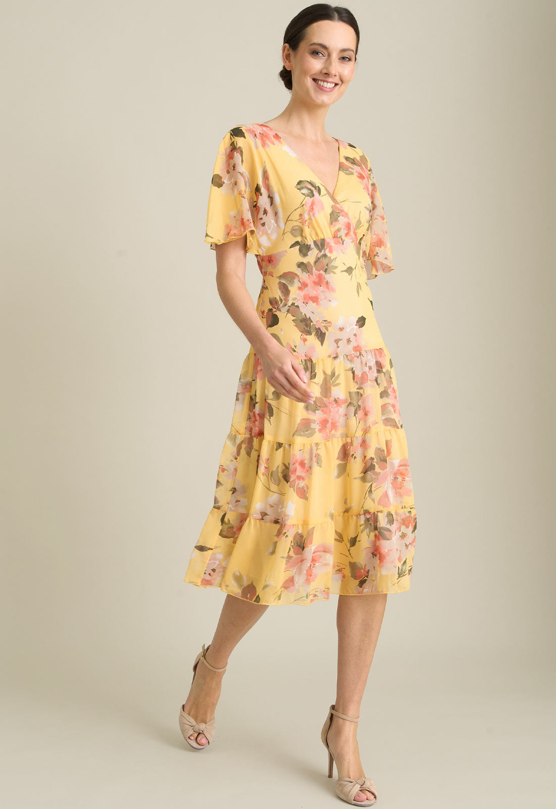 Woman wearing a yellow floral dress against a neutral background