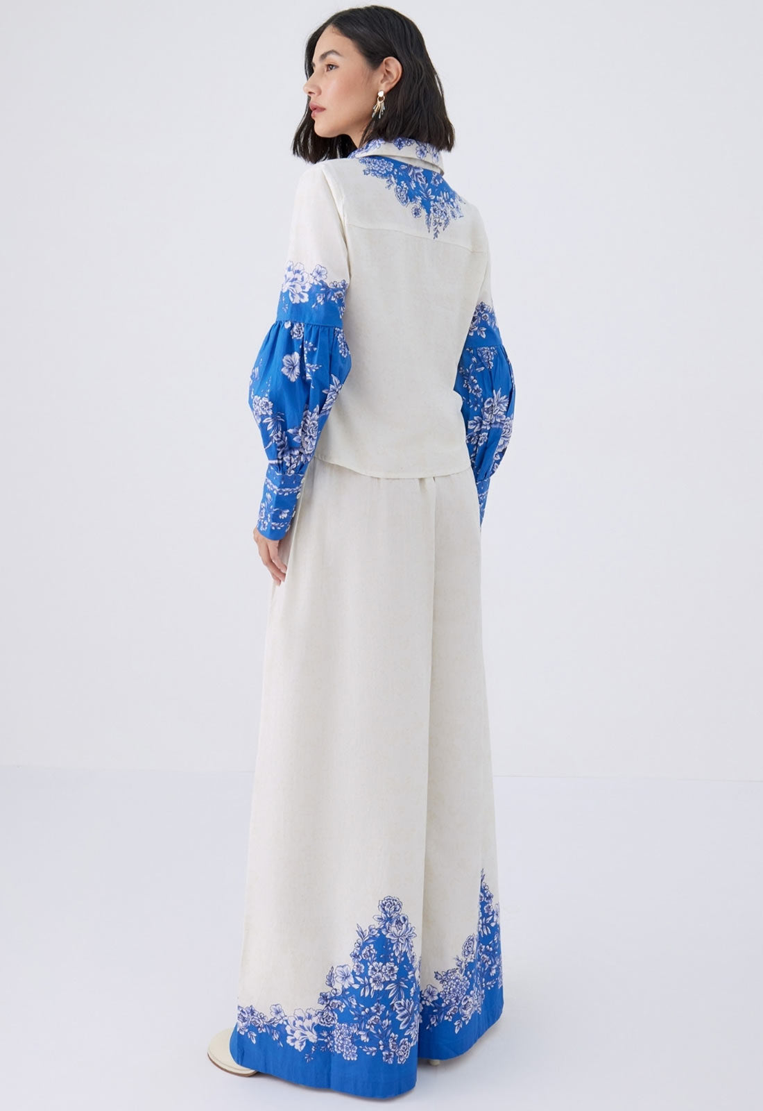 Woman wearing a white outfit with blue floral embroidery on a white background