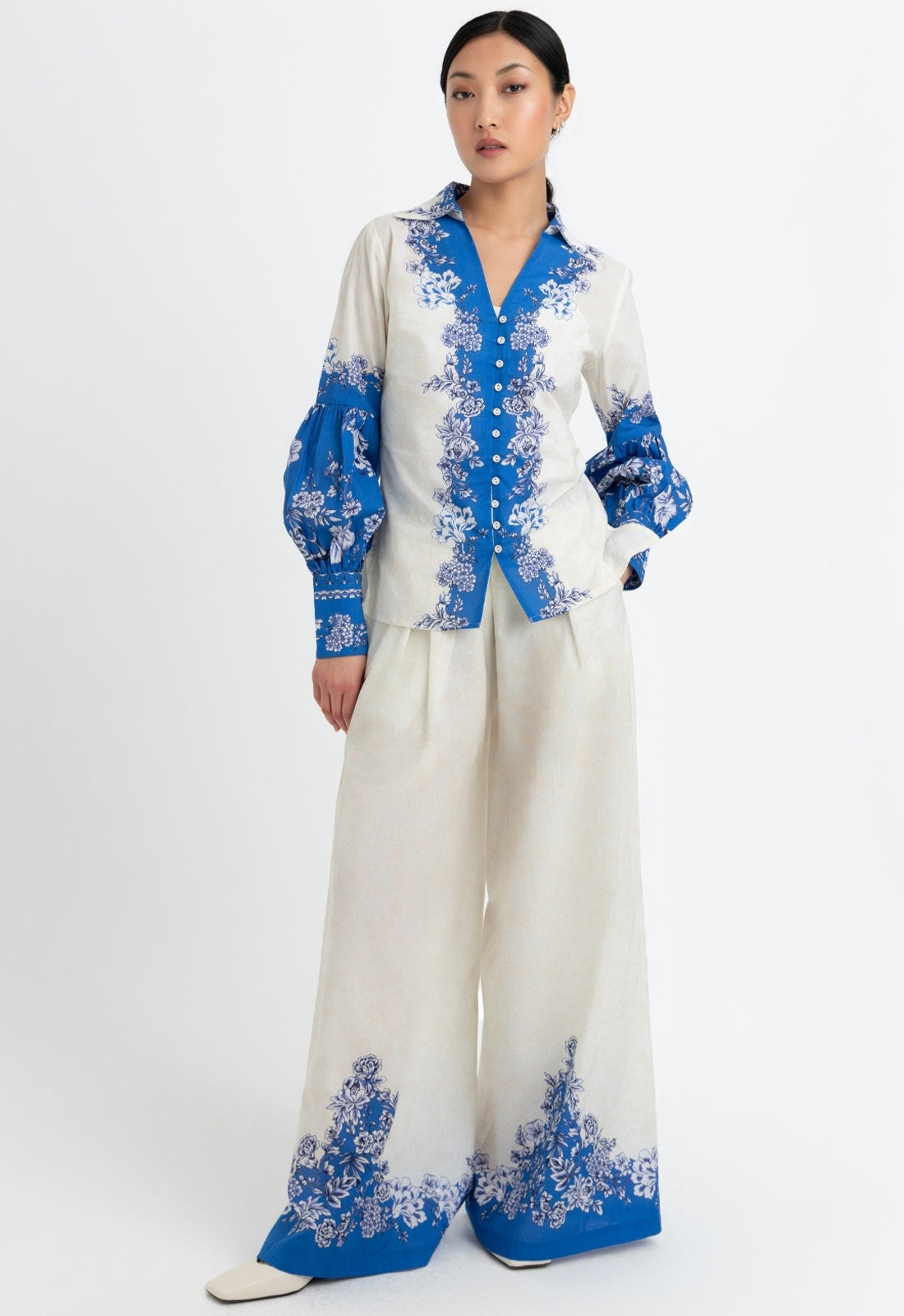 Woman wearing a white outfit with blue floral embroidery on a white background
