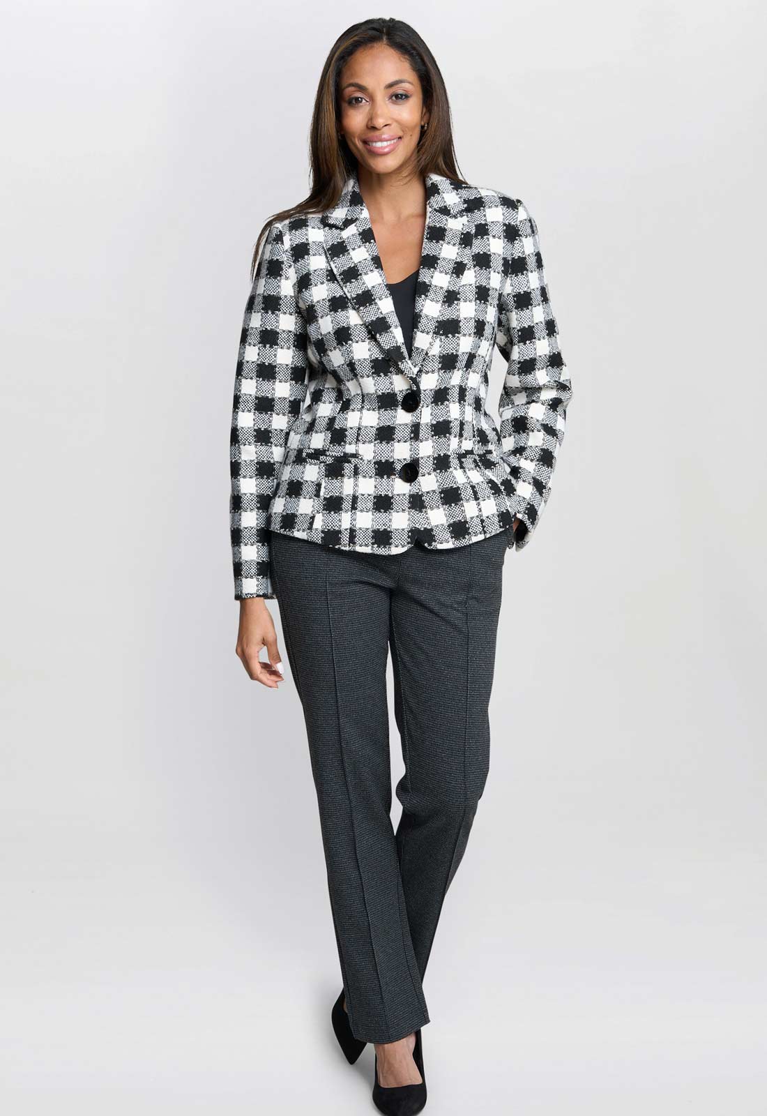 Woman wearing a black and white checkered blazer and dark gray pants on a white background