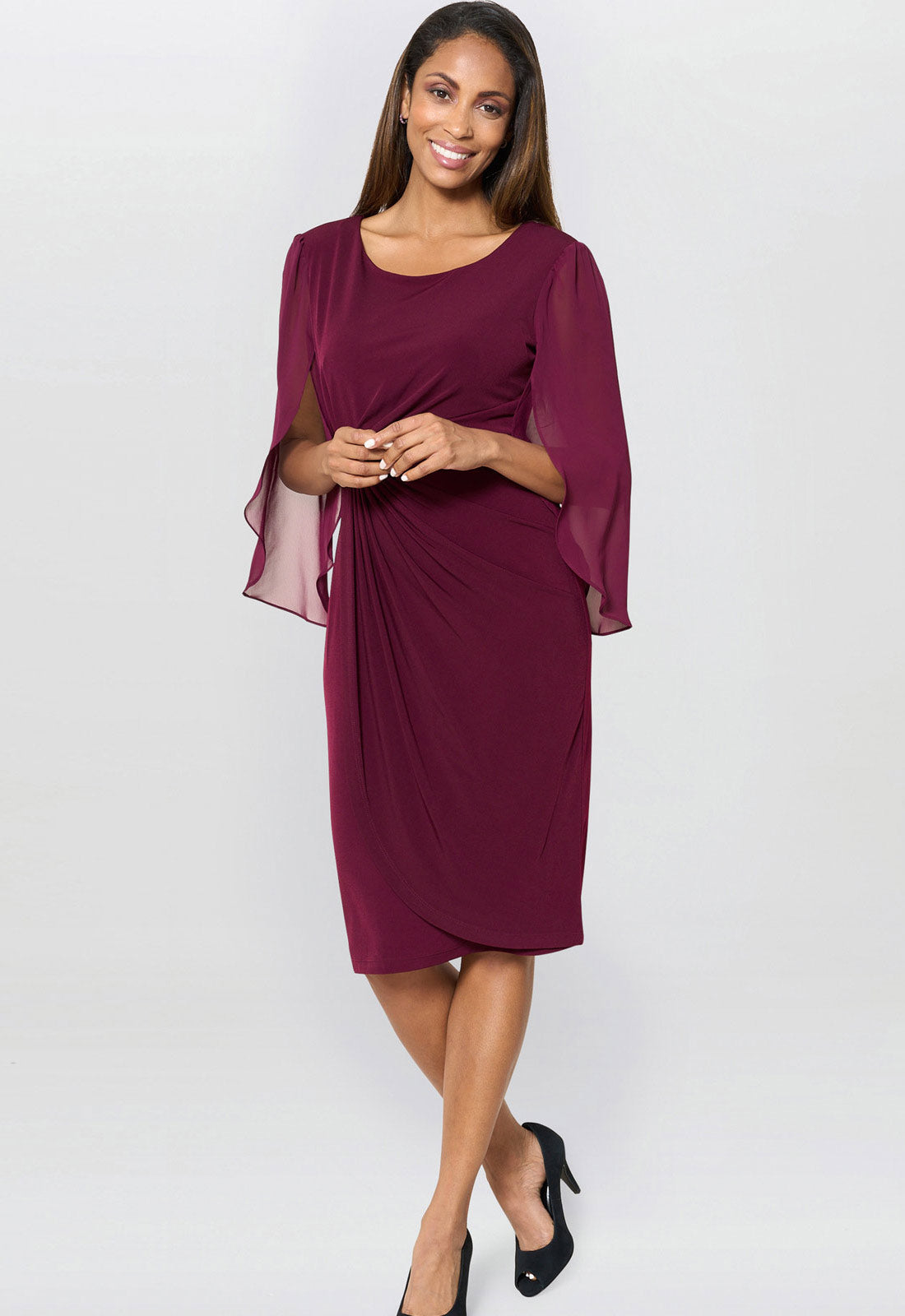 Woman wearing a burgundy dress with sheer sleeves on a white background
