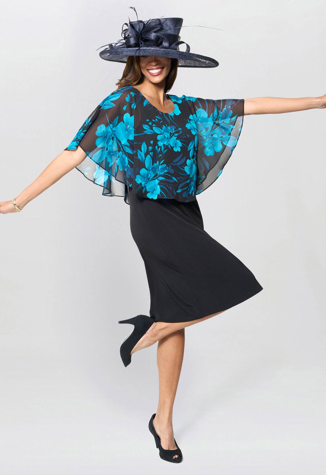 Woman wearing a black dress with blue floral pattern and a matching hat on a white background