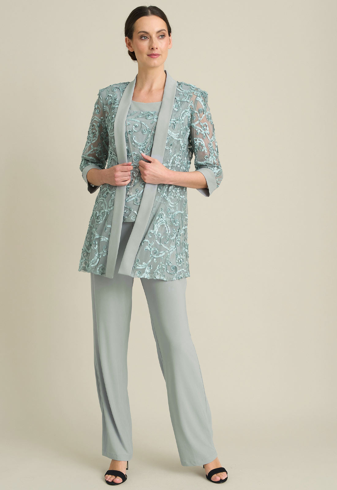 Woman wearing a light blue floral jacket with a matching top and gray pants on a beige background