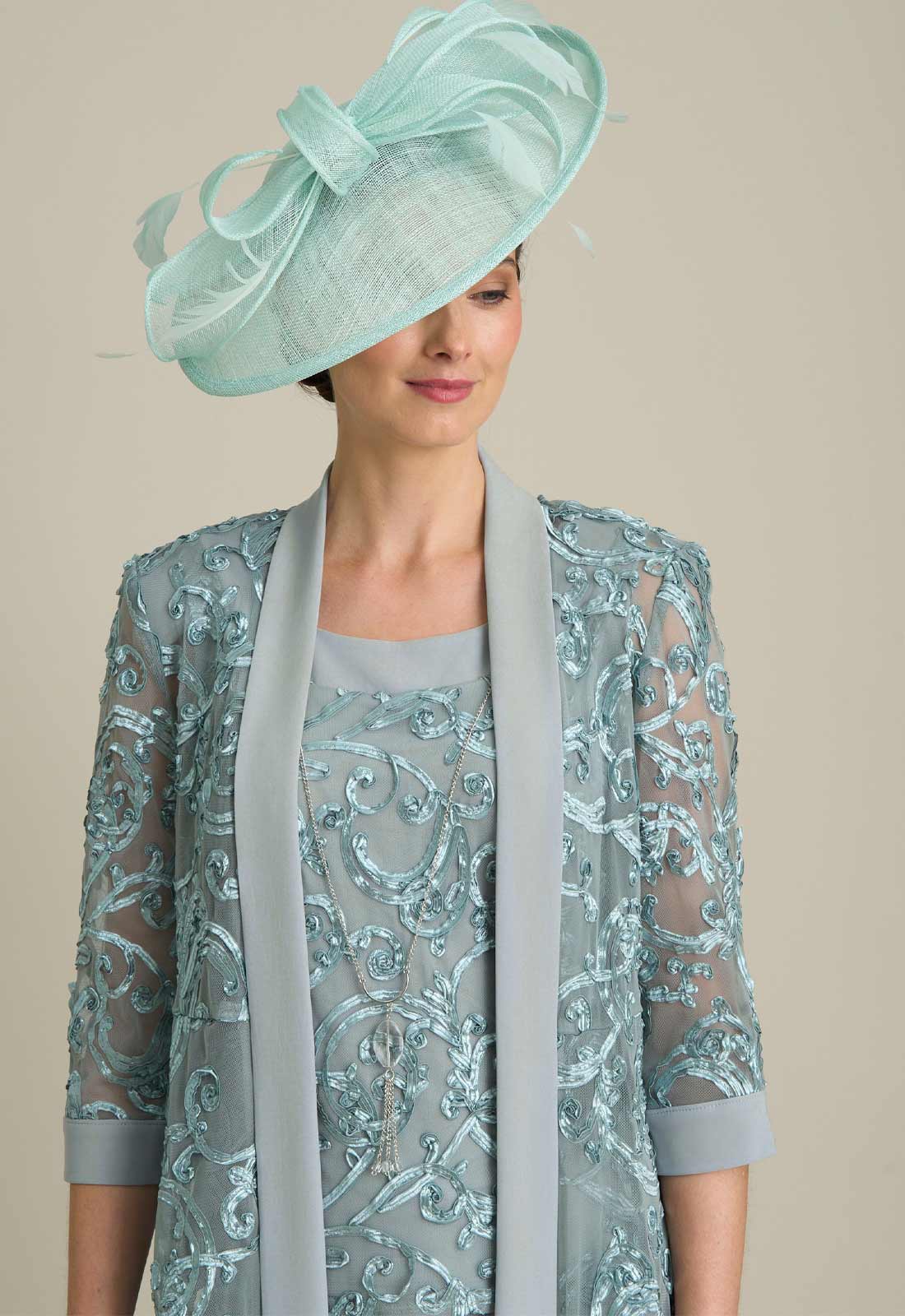Woman wearing a light blue lace dress with a matching hat on a beige background
